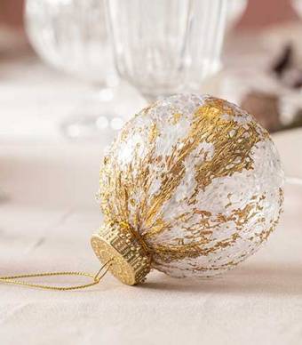 Bola de natal transparente com desenhos em dourado em cima de uma mesa